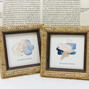 Peut inclure: Deux petites impressions d'art encadrées carrées. L'une présente des cercles d'aquarelle abstraits en or, rose et bleu. L'autre présente des coups de pinceau bleus, beiges et dorés. Les deux sont étiquetés "MACKENZIE FRAMES."