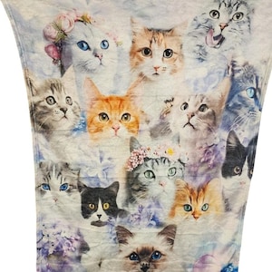 May include: A soft, light blue blanket featuring a collage of cat faces in various colors and patterns. Some cats wear floral crowns. The blanket is a cozy home decor item.