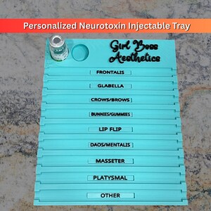 May include: A light blue rectangular tray with a circular vial holder and the text Girl Boss Aesthetics. It features horizontal slots labeled Frontalis, Glabella, Crows/Brows, Bunnies/Gummies, Lip Flip, Daos/Mentalis, Masseter, Platysmal, and Other.