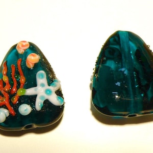 May include: Two teal blue glass beads, one with a starfish and coral design, the other plain.