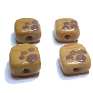 May include: Four square-shaped ceramic beads with a light brown glaze and brown paw print designs.