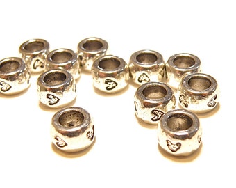 May include: A group of silver-toned metal beads with a heart design. The beads are round and have a hole in the center.