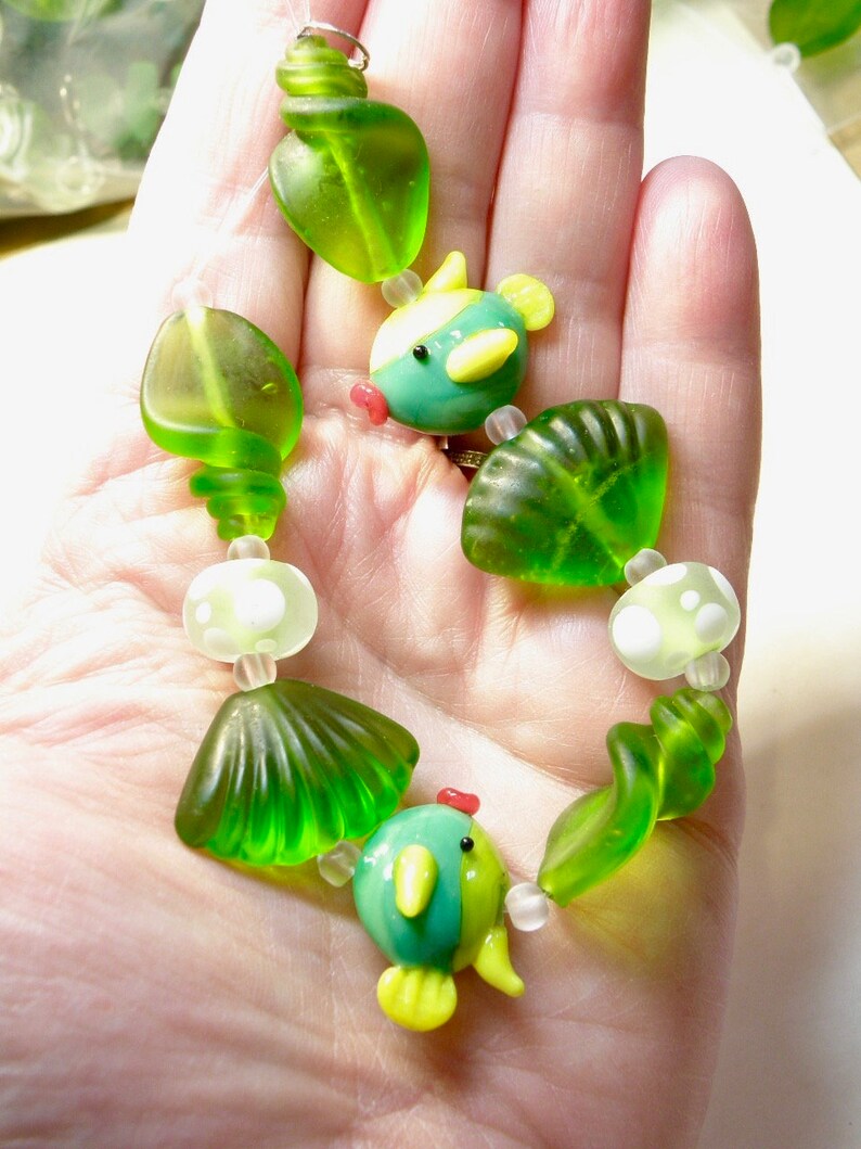 May include: A green and blue glass bead necklace with a seahorse and shell design.