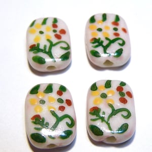 May include: Four white ceramic beads with a floral design. The beads are painted with green leaves, yellow flowers, and red dots.