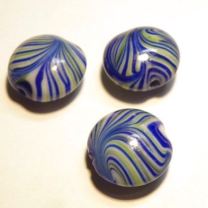 May include: Three oval-shaped glass beads with a swirl pattern. The beads feature a combination of blue, green, and white colors. Each bead has a small hole, suggesting they are for stringing. The beads are likely for jewelry making or crafts.