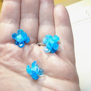 Puede incluir: Tres peque&ntilde;os abalorios de flores de vidrio azul y blanco. Los abalorios tienen la forma de una flor con cinco p&eacute;talos y un centro.