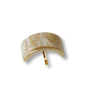 Puede incluir: Un botón decorativo de forma semicircular, de color dorado, con un diseño marmoleado blanco y beige.