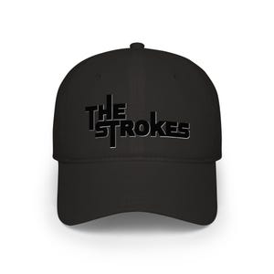 Puede incluir: Gorra de béisbol negra con el nombre de la banda "The Strokes" en una fuente audaz y estilizada. El texto es negro con un contorno blanco, creando un contraste llamativo con el color negro sólido de la gorra. Un accesorio clásico y casual.