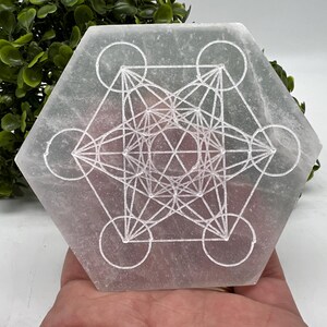 Può includere: Piatto di ricarica in selenite bianca con un disegno geometrico inciso sulla superficie. Il disegno è un motivo di geometria sacra noto come Fiore della Vita.