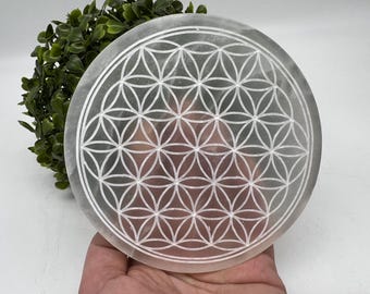 May include: A white selenite crystal disc with a carved flower of life pattern. The disc is approximately 6 inches in diameter.