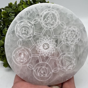 Peut inclure: Plaque de recharge en sélénite blanche avec sept symboles de chakras gravés à la surface. La plaque est ronde et a une finition lisse et polie.