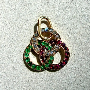 May include: A gold pendant featuring three interlocking circular rings, each set with small round gemstones. One ring contains clear white stones, another features vibrant green stones, and the third is set with deep red stones, topped with a gold bail.