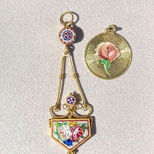 Puede incluir: Dos colgantes dorados. Uno es un dise&ntilde;o ornamentado con un patr&oacute;n floral de mosaico y una parte superior circular con un dise&ntilde;o rojo, blanco y azul. El otro es un colgante redondo con una rosa rosa y un tallo verde.