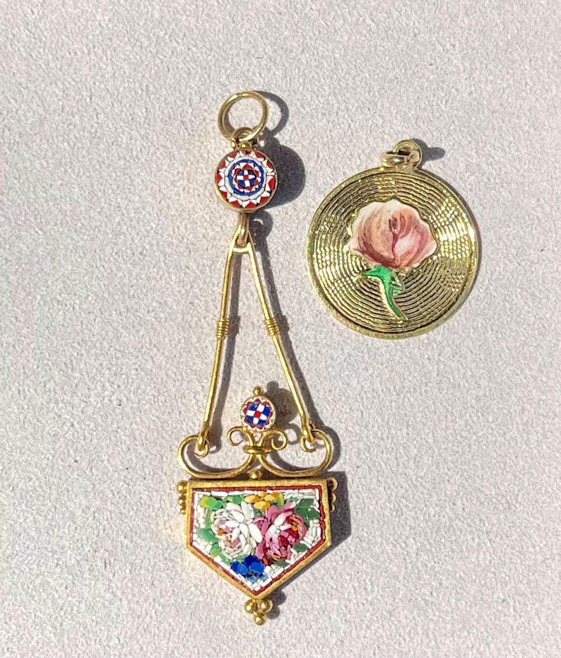 Puede incluir: Dos colgantes dorados. Uno es un dise&ntilde;o ornamentado con un patr&oacute;n floral de mosaico y una parte superior circular con un dise&ntilde;o rojo, blanco y azul. El otro es un colgante redondo con una rosa rosa y un tallo verde.