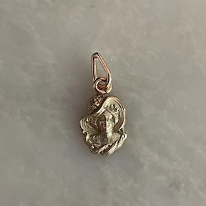 May include: A silver-toned pendant featuring a woman's profile wearing a wide-brimmed hat. The pendant has a detailed, Art Nouveau style design with a loop for attaching to a chain. The woman's face is visible, and the hat has decorative elements.