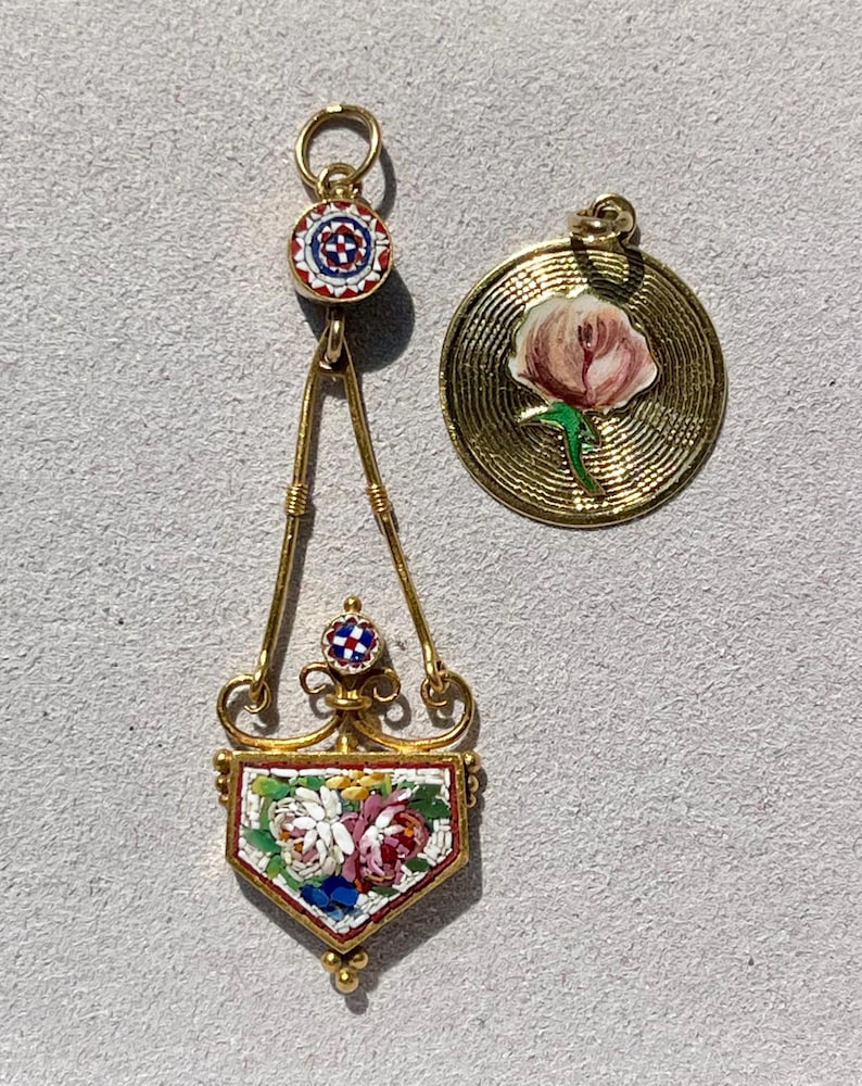 Puede incluir: Dos colgantes de oro. Uno es un dise&ntilde;o largo y ornamentado con un mosaico floral. El otro es un colgante redondo con un dise&ntilde;o de flor rosa. Ambos tienen lazos dorados para colgar.