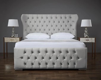 May include: A gray upholstered bed frame with a tufted headboard and footboard. The bed frame has a winged headboard and a low profile footboard. The bed frame is sitting on a wooden floor.