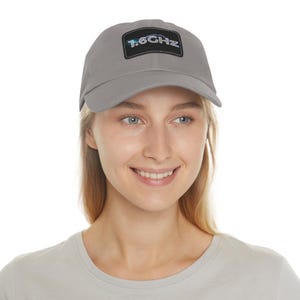 May include: A gray baseball cap with a rectangular patch featuring the text "1.6GHz" in a gradient color scheme. The cap is made of a soft material and has a curved brim.