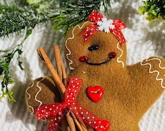 May include: A brown gingerbread person ornament with a red and white polka dot bow, two cinnamon sticks, and red heart accents.