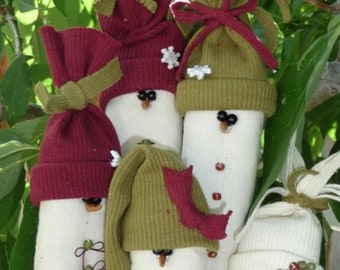 May include: Four handmade snowman decorations made from white fabric with green and red felt hats and embellishments. The decorations are decorated with beads and have a rustic, homemade look.