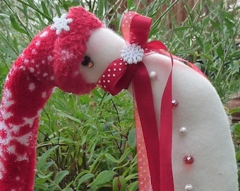 May include: A white felt snowman ornament with a red and white knit stocking hat and a red ribbon with white polka dots. The snowman has a red nose and white buttons.