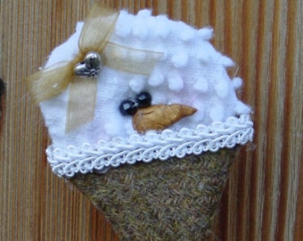 May include: A white felt snowman ornament with a brown felt nose, black button eyes, and a gold ribbon bow. The snowman is sitting on a brown felt cone.