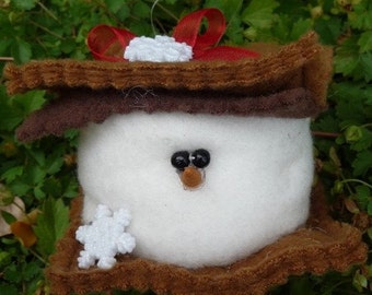 May include: A handmade snowman ornament with a white body, black bead eyes, and a small orange nose. The snowman is wearing a brown felt hat and a red ribbon. A white glitter snowflake is attached to the base.