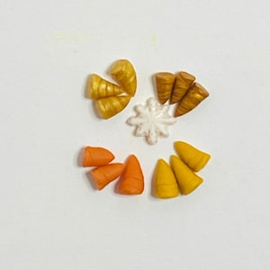 May include: A collection of small, colorful, fondant carrots and corn on the cob, perfect for decorating cakes or cupcakes. The fondant pieces are arranged in a circle around a white snowflake.