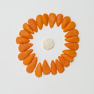 May include: A circle of orange fondant carrots arranged around a white fondant ball. The carrots are all the same size and shape, and they are arranged in a symmetrical pattern.