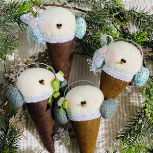 May include: Four handmade felt snowman ornaments shaped like ice cream cones. Each snowman has a white felt face, black eyes, and a red nose. They are wearing blue and white patterned hats and scarves.