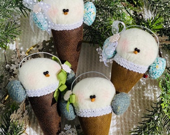 May include: Four handmade felt snowman ornaments shaped like ice cream cones. Each snowman has a white felt face, black eyes, and a red nose. They are wearing blue and white patterned hats and scarves.