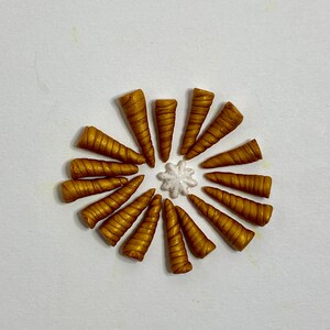 May include: A collection of 15 gold unicorn horn shaped charms arranged in a circle around a white star-shaped charm.