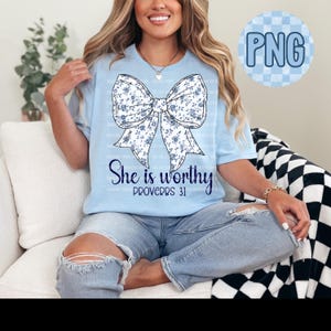 May include: A light blue t-shirt with a white floral bow and the text "She is worthy Proverbs 31" in navy blue.