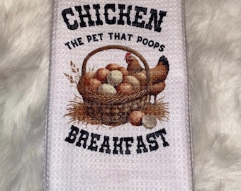 Pode incluir: Toalha de cozinha branca com textura de waffle. Apresenta um gráfico de uma cesta cheia de ovos, uma galinha e o texto "CHICKEN THE PET THAT POOPS BREAKFAST" em preto.