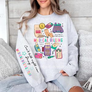 May include: A light grey sweatshirt featuring a colourful graphic design related to medical billing. The design includes illustrations of a calculator, payment card, and a bill. The sleeve has text that says "MEDICAL BILLING STUFF".