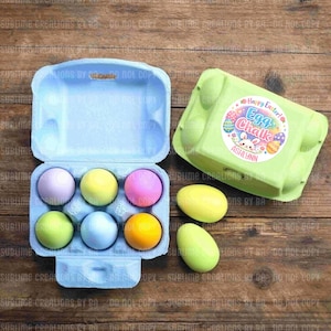 May include: A light blue egg carton holds six pastel-colored eggs: lavender, yellow, pink, green, blue, and orange. A green egg carton with a "Happy Easter! Egg Chalk" sticker is nearby, along with two loose eggs.