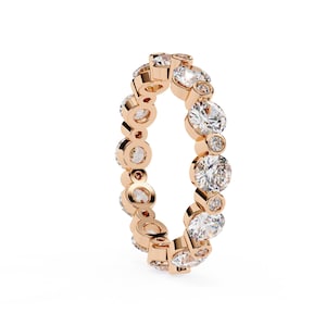 Op de afbeelding: Eeuwigheidsring van roségoud met een doorlopende rij ronde en kleinere accentdiamanten. Het ontwerp van de ring toont een mix van grotere en kleinere stenen, wat zorgt voor een sprankelende, elegante uitstraling.
