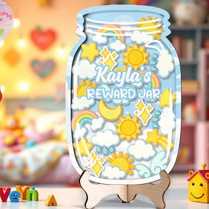 Pode incluir: Um frasco de recompensa de madeira com um fundo de céu azul, apresentando nuvens, arco-íris, estrelas e sóis. O frasco está rotulado como "Kayla's REWARD JAR" e é exibido em um suporte de madeira. A imagem também inclui o texto "Size XL Best seller Stand included".