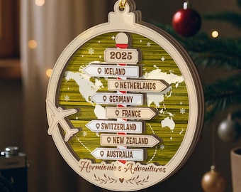 May include: Wooden Christmas ornament with a world map design and directional signs pointing to various countries. The ornament includes the year 2025 and the text "Hermionie's Adventures". A small airplane graphic is also present.