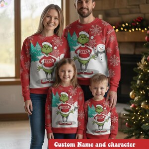 May include: A family of four wearing matching red Christmas jumpers. Each jumper features a Grinch character design with a Santa hat, a red and white striped shirt, and a snowman. The jumpers have a snowflake pattern and the text "Custom Name and character".