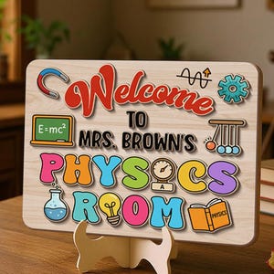 May include: A wooden sign with the words "Welcome to Mrs. Brown's Physics Room" in colorful letters. The sign includes science-themed graphics like a lightbulb, a beaker, and the equation E=mc². It is displayed on a wooden stand.