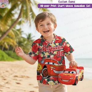 May include: A child's red Hawaiian shirt with a floral design and a Lightning McQueen graphic. The shirt features short sleeves and the text "McQueen 00". The child is holding a red Lightning McQueen toy car.