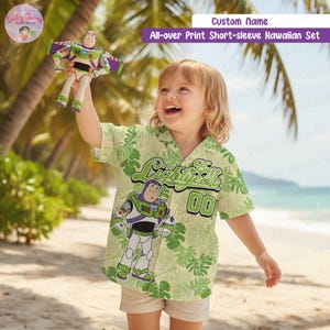 May include: A child's light green Hawaiian shirt featuring a Buzz Lightyear design and the text "Lightyear 00". The shirt has a tropical leaf pattern. The child is holding a Buzz Lightyear toy on a beach.