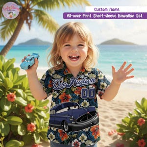 May include: A child's navy blue short-sleeved Hawaiian shirt featuring a car graphic and the text "Doc Hudson 00". The shirt is decorated with a floral pattern of orange and white flowers. The child is holding a blue toy car.