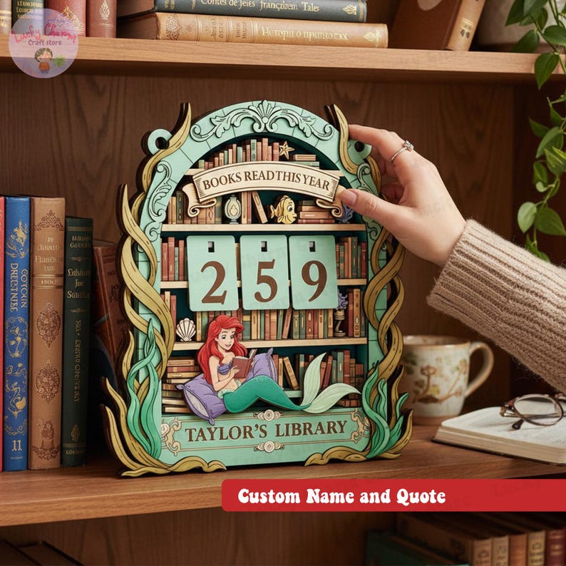 May include: A wooden bookshelf-shaped calendar with the text "BOOKS READ THIS YEAR" and the numbers "259". The design includes a mermaid reading a book, with the text "TAYLOR'S LIBRARY". The calendar is on a wooden shelf.