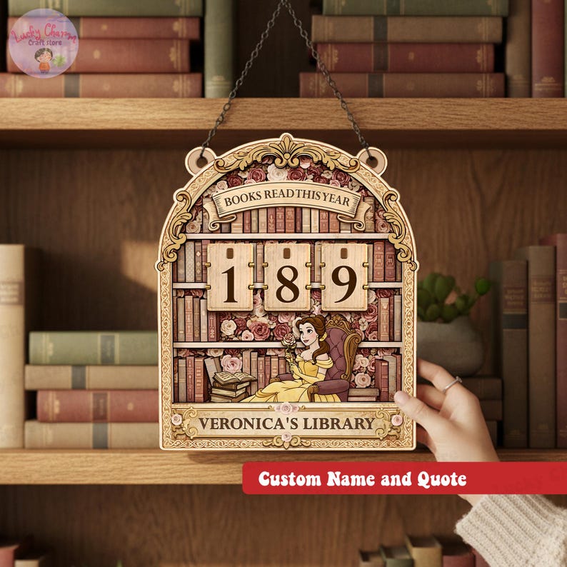 May include: Wooden wall hanging with a library theme. The sign features a decorative frame with the words "BOOKS READ THIS YEAR" at the top. The center displays the numbers "189" and a cartoon of a woman in a yellow dress. The sign reads "VERONICA'S LIBRARY".