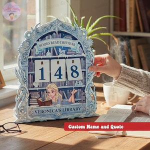 May include: A light blue wooden bookshelf-shaped calendar with the text "BOOKS READ THIS YEAR" and the numbers "148". The bottom of the calendar reads "VERONICA'S LIBRARY". The calendar has a decorative frame with floral and snowflake designs.