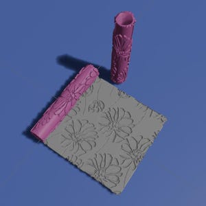Puede incluir: Dos rodillos rosas con estampado floral y un cuadrado gris texturizado con un patrón de margaritas. Estas herramientas están diseñadas para crear patrones decorativos en superficies.
