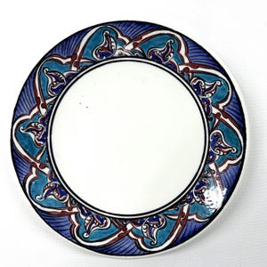Pode incluir: Um prato de cerâmica branco com uma borda estampada em azul e turquesa. O padrão apresenta desenhos florais intrincados com acentos vermelhos.