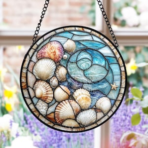 Puede incluir: Una vidriera redonda con un diseño de conchas marinas. La ventana tiene un marco de metal negro y está suspendida por una cadena. El diseño incluye varias conchas en tonos marrón, blanco y rosa, sobre un fondo azul y turquesa.